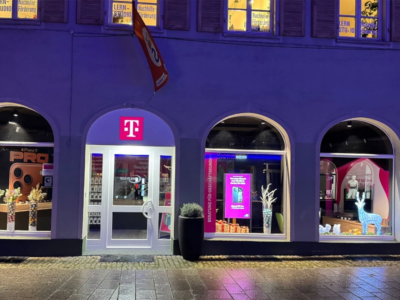 Beleuchtetes Telekom-Shop-Schaufenster mit Smartphone-Werbung und Dekoration bei Nacht.